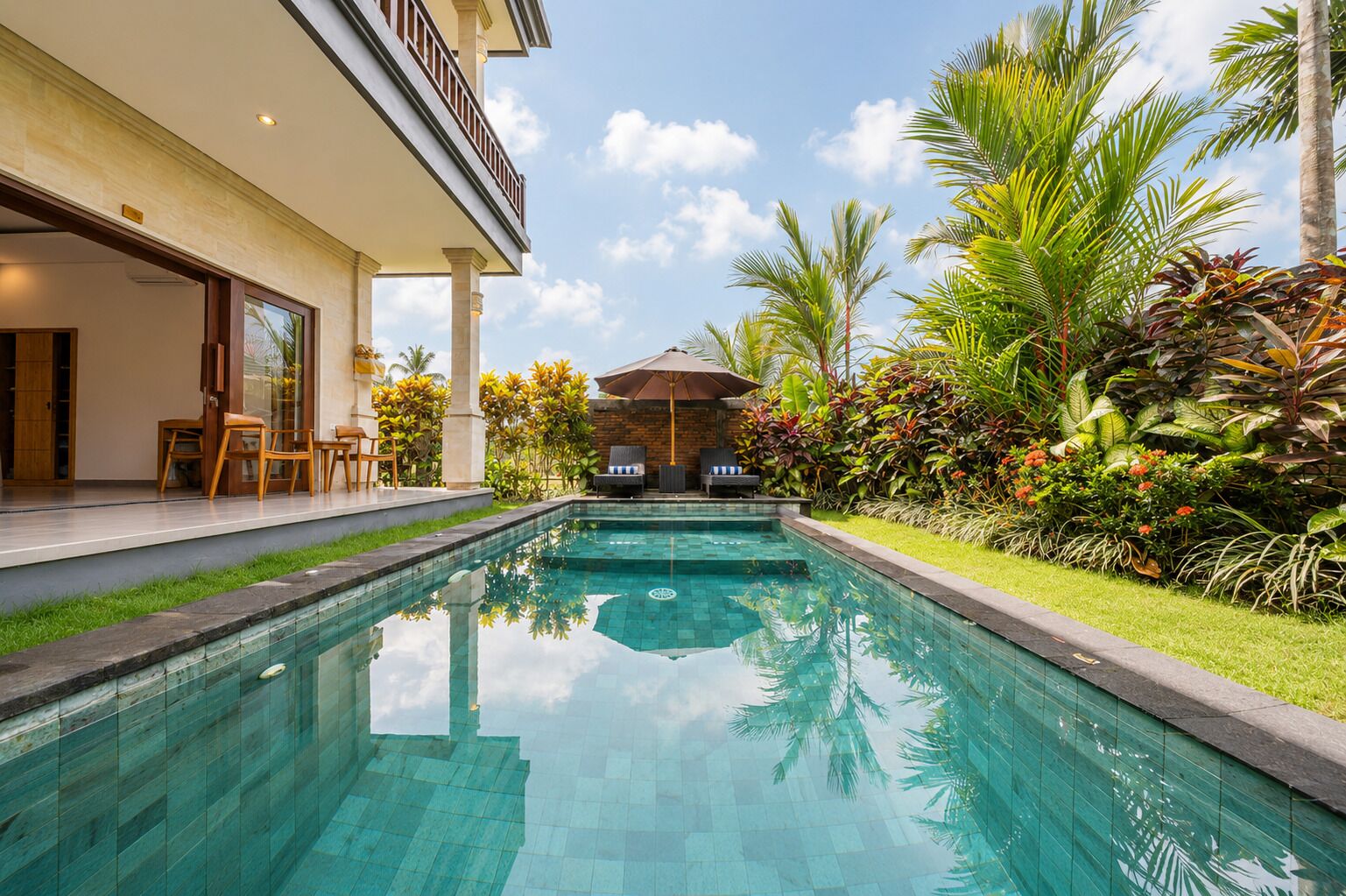 Una piscina con vista despejada al cielo, rodeada de abundante vegetación y un edificio con balcón.