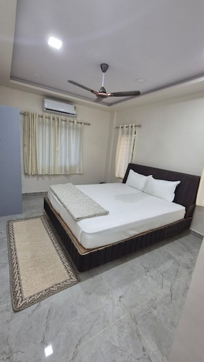 Un dormitorio con cama, ventilador de techo, aire acondicionado y ventana con cortinas.