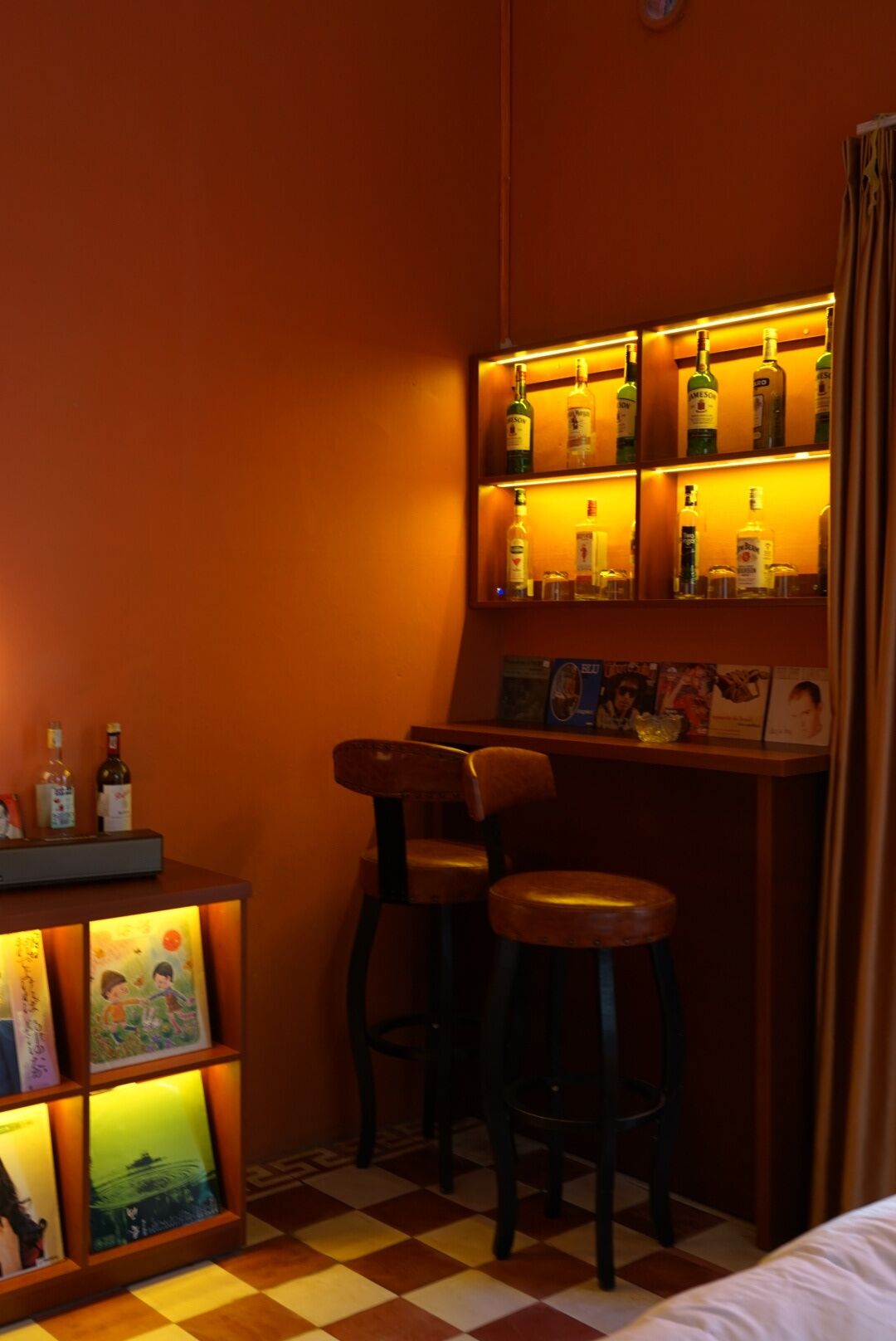 Un espace bar avec des tabourets, une étagère remplie de bouteilles et des tableaux encadrés.