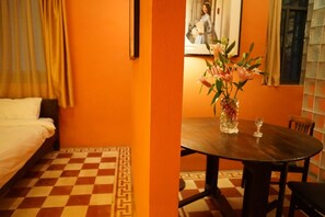 Een kamer met een geruit vloerkleed, een bed, een tafel met een bloevas en een foto in een lijst aan de muur.