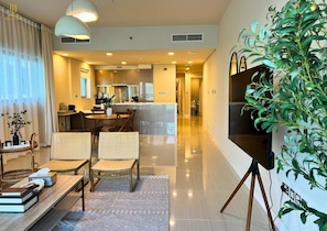 A modern hotel room with a dining area, a kitchen, and a large plant. - Seaside 2BR Escape in Al Reem (Abu Dhabi)