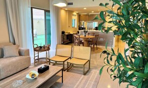 A modern hotel room with a sofa, two wicker chairs, a dining table, and a kitchen area visible through an open door. - Spacious 2BR with Direct Beach Access in Al Reem (Abu Dhabi)