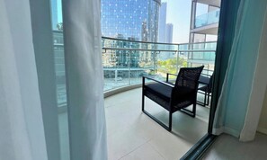 Un balcon avec une chaise et une table, une rambarde en verre et une vue sur de hauts immeubles.