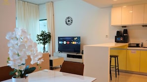 Una habitación de hotel moderna con zona de comedor, televisión, reloj y kitchenette.