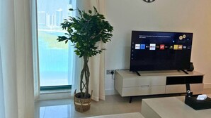 Una sala de estar moderna con un gran ventanal, una planta en maceta, un televisor de pantalla plana, un reloj y un mueble blanco minimalista.