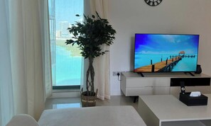 Una sala de estar moderna con televisor, planta en maceta, ventana con cortinas y vista a un muelle.