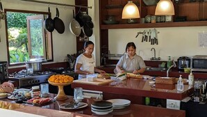Una cocina con una isla central, ollas colgantes y una ventana con follaje visible.
