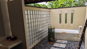 Un baño con bañera, zona de ducha y un pequeño jardín con plantas y piedras.