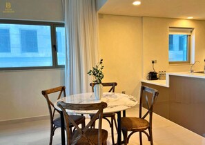 Una cocina moderna con encimera de mármol, sillas de madera, un jarrón con flores y una ventana con cortinas.