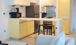 Una cocina moderna con una isla central, taburetes de bar y un sofá blanco en la sala de estar.