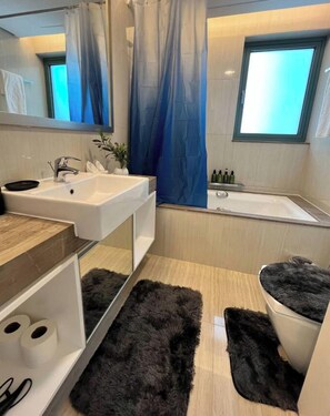 Un baño moderno con un lavamanos blanco, una bañera, un espejo grande y una alfombra negra.