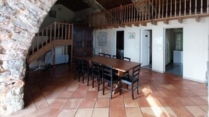 Ein geräumiger Essbereich mit einem langen Holztisch und Stühlen, einer Steinsäule und einer Holztreppe, die zu einer oberen Ebene führt.
