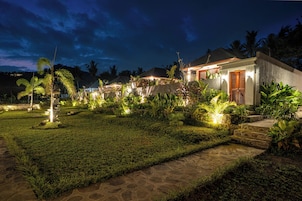 Un resort bien iluminado con un camino de piedra que lleva a un edificio, rodeado de exuberante vegetación y palmeras.