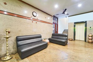 A lobby with two black sofas, a wall clock, a ceiling fan, and an elevator. - Itsy Hotels R S Bhavan, 2 km from MIT Gate (Manipal)