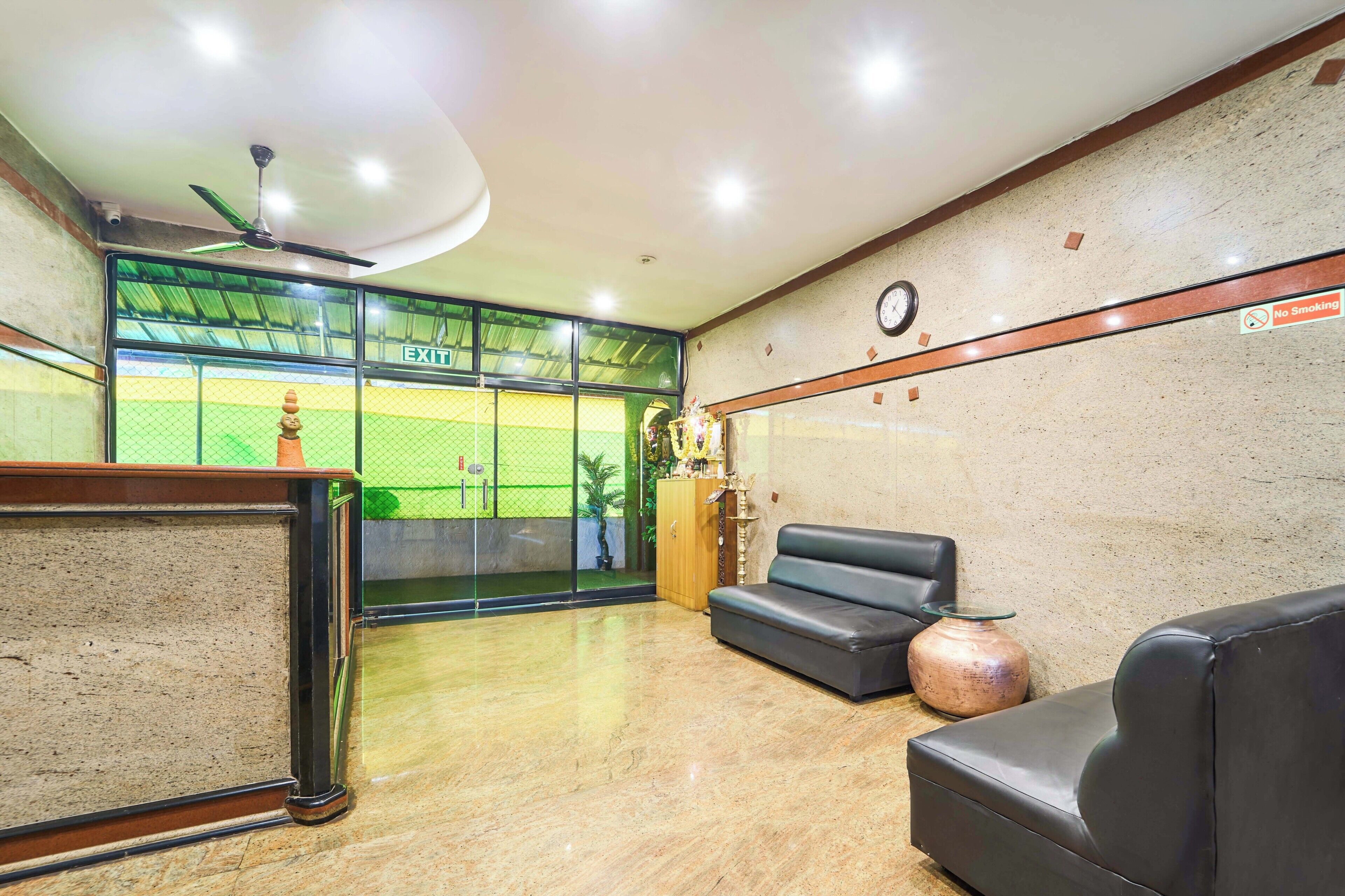 A lobby with a reception desk, a clock, a 'No Smoking' sign, a sofa, and a large window with a view of a sports field.