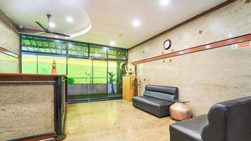 A lobby with a reception desk, a clock, a 'No Smoking' sign, a sofa, and a large window with a view of a sports field.