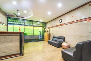 A lobby with a reception desk, a clock, a 'No Smoking' sign, a sofa, and a large window with a view of a sports field. - Itsy Hotels R S Bhavan, 2 km from MIT Gate (Manipal)