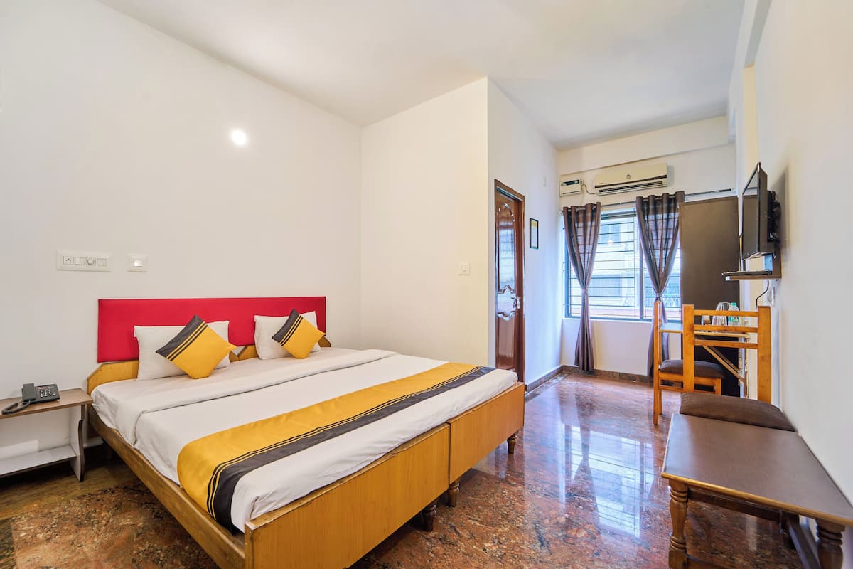 A hotel room with a bed, a desk, a chair, and an air conditioning unit.