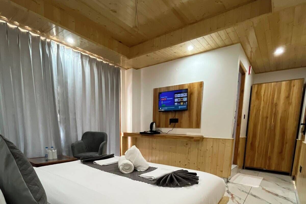 Habitación de hotel con cama, televisión montada en la pared, techo de madera y piso de mármol.