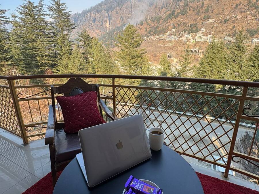 A balcony with a laptop, a plate of chocolate, and a cup of coffee.