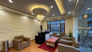 A hotel lobby with a reception desk, seating area, chandelier, and large windows. - Hotel The Travica Kasol (Kasol)