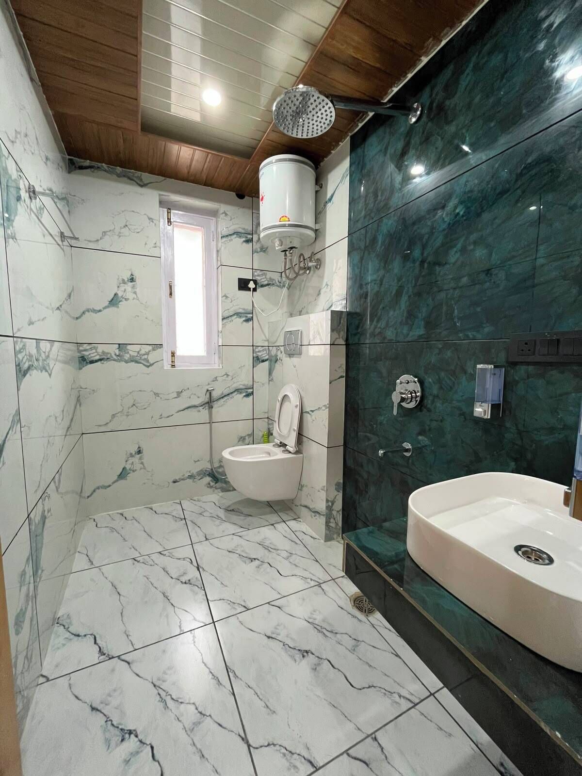 A bathroom with a toilet, shower, and sink, marble tiles, and a wooden ceiling.