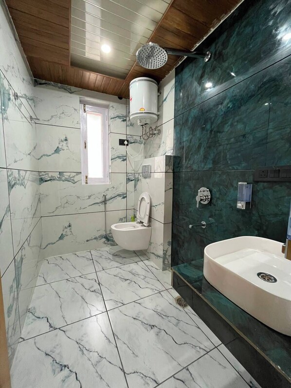 A bathroom with a toilet, shower, and sink, marble tiles, and a wooden ceiling. - Hotel The Travica Kasol (Kasol)