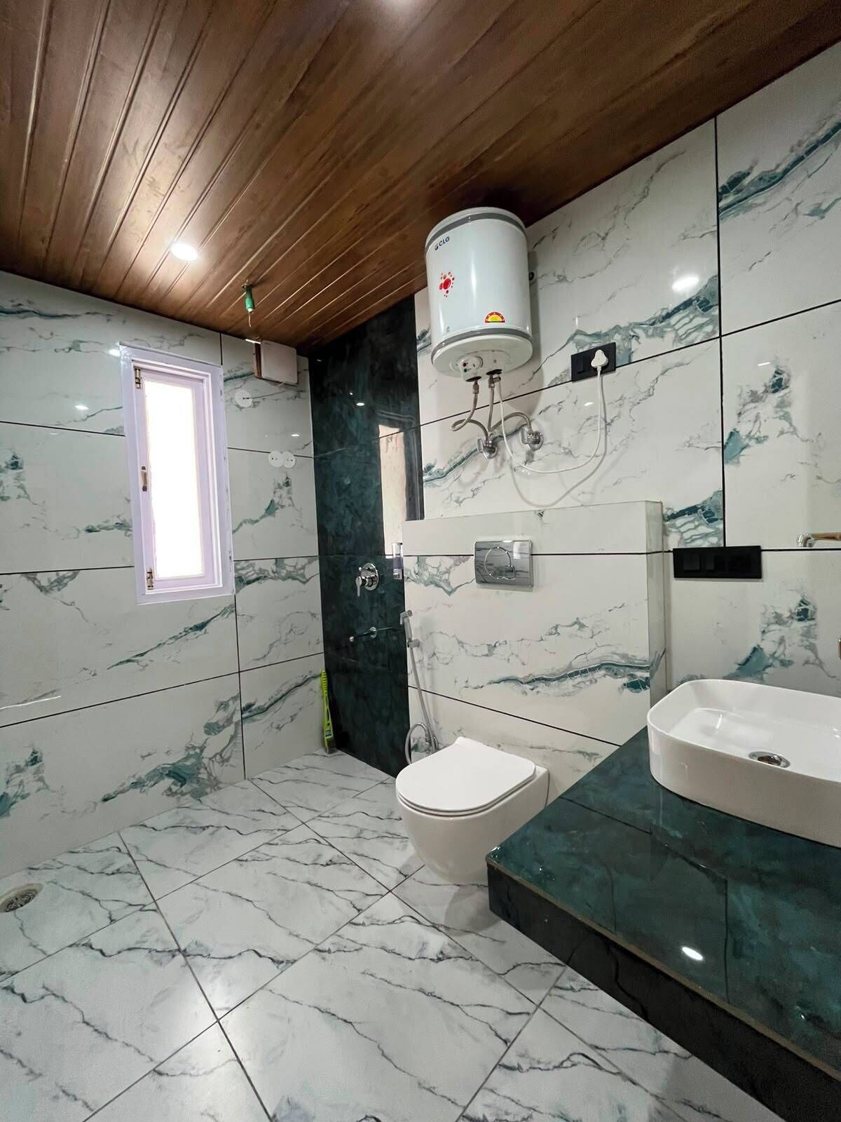 Un baño con inodoro, bidé y lavamanos, azulejos de mármol y techo de madera.