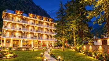 Un hotel de varios pisos con balcones, fachada de piedra y un camino de jardín bien iluminado.