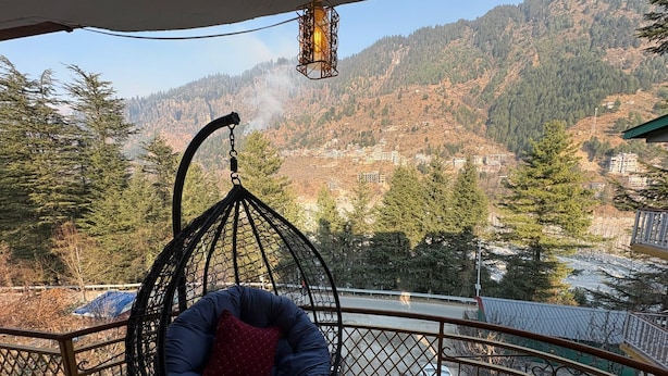 A hanging chair with a cushion, a table with two cups, and a view of a mountainous landscape. - Hotel The Travica Kasol (Kasol)