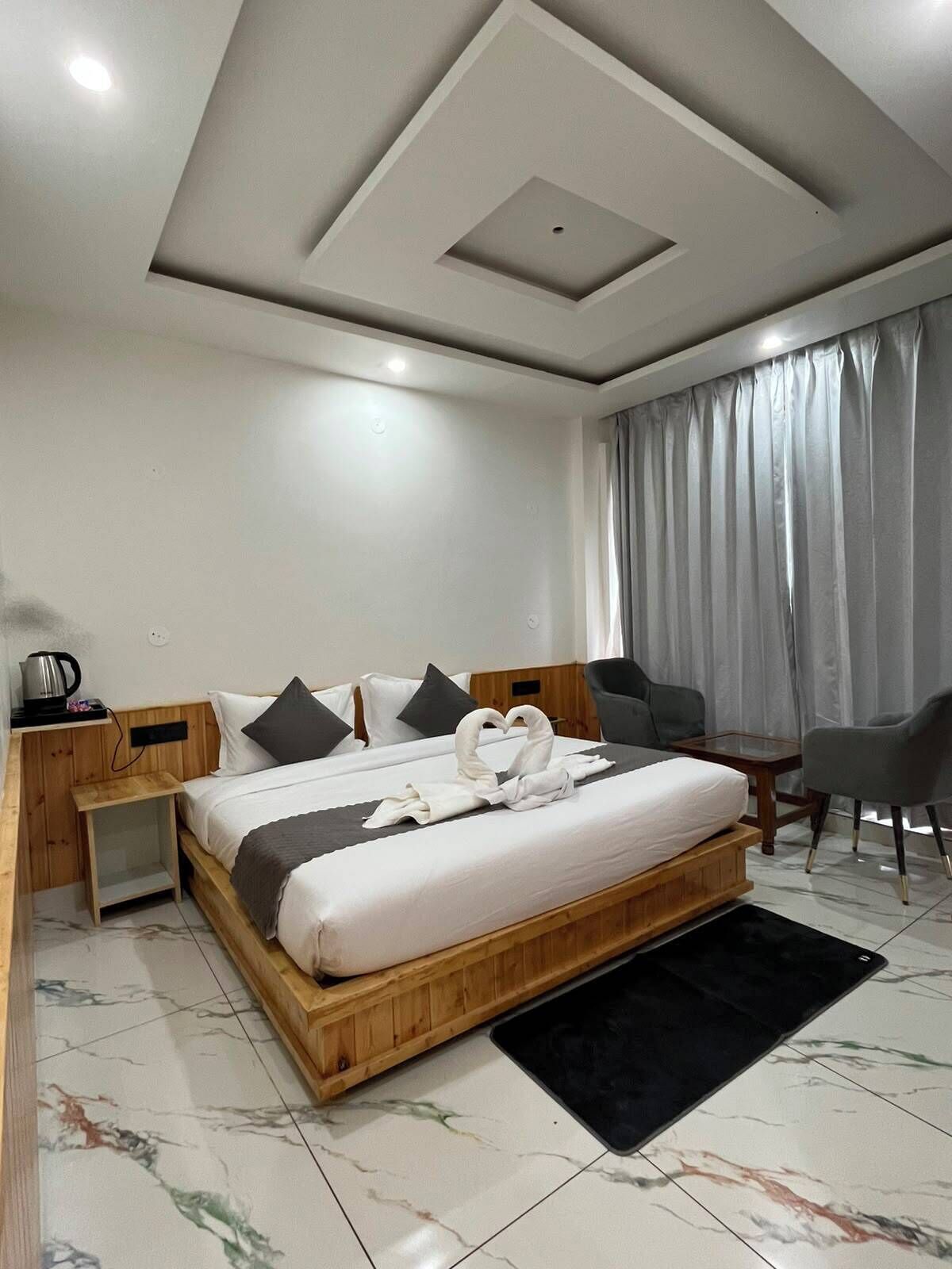 A modern hotel room with a wooden bed, grey curtains, a small table, and a chair.