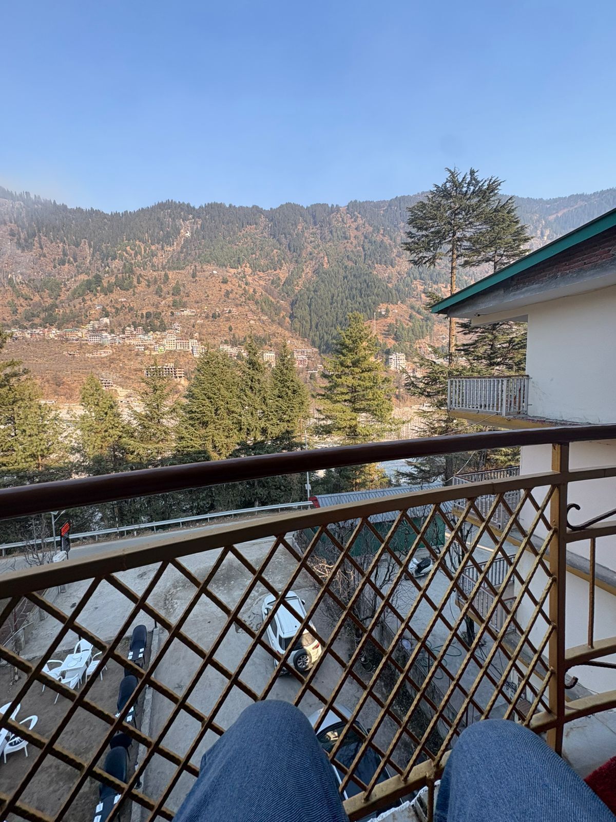 Un balcon donnant sur un paysage montagneux, une voiture garée et un bâtiment doté d’un toit végétalisé.