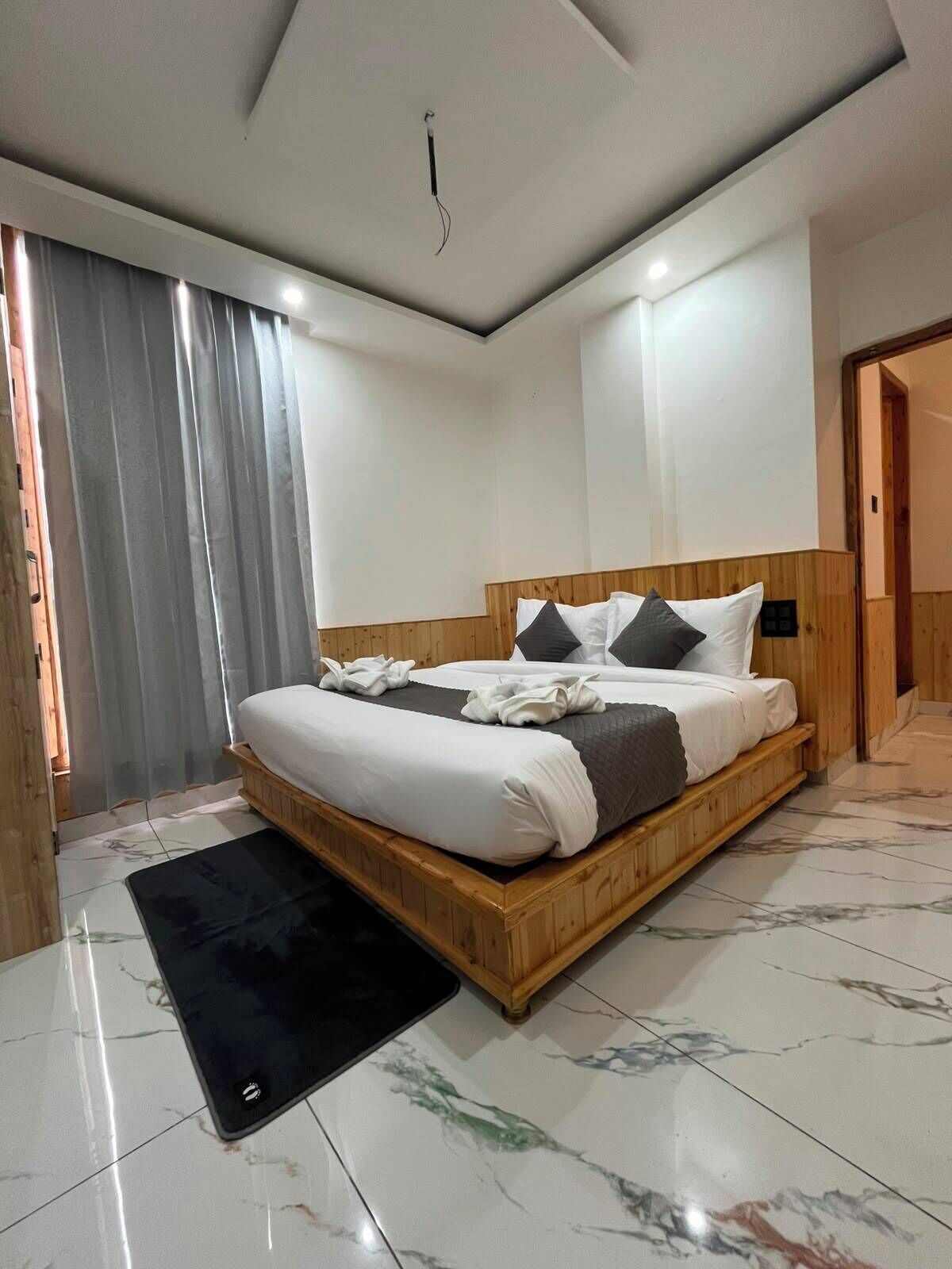 Un dormitorio moderno con una cama de madera, ropa de cama blanca, una alfombra negra y suelo de mármol.