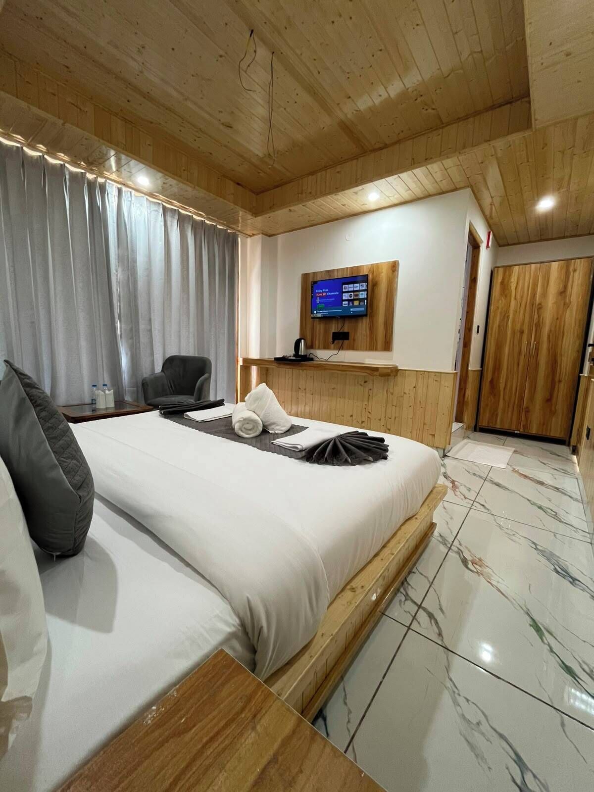 Une chambre d’hôtel avec un lit, un téléviseur fixé au mur, un plafond en bois et une porte.