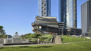 Un edificio moderno con fachada de vidrio, un letrero que dice 'Melbourne Square' y un área ajardinada con escaleras que conducen a la entrada.