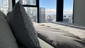 Una cama con ropa de cama a rayas y una almohada con notas escritas a mano, una ventana con vista a la ciudad.