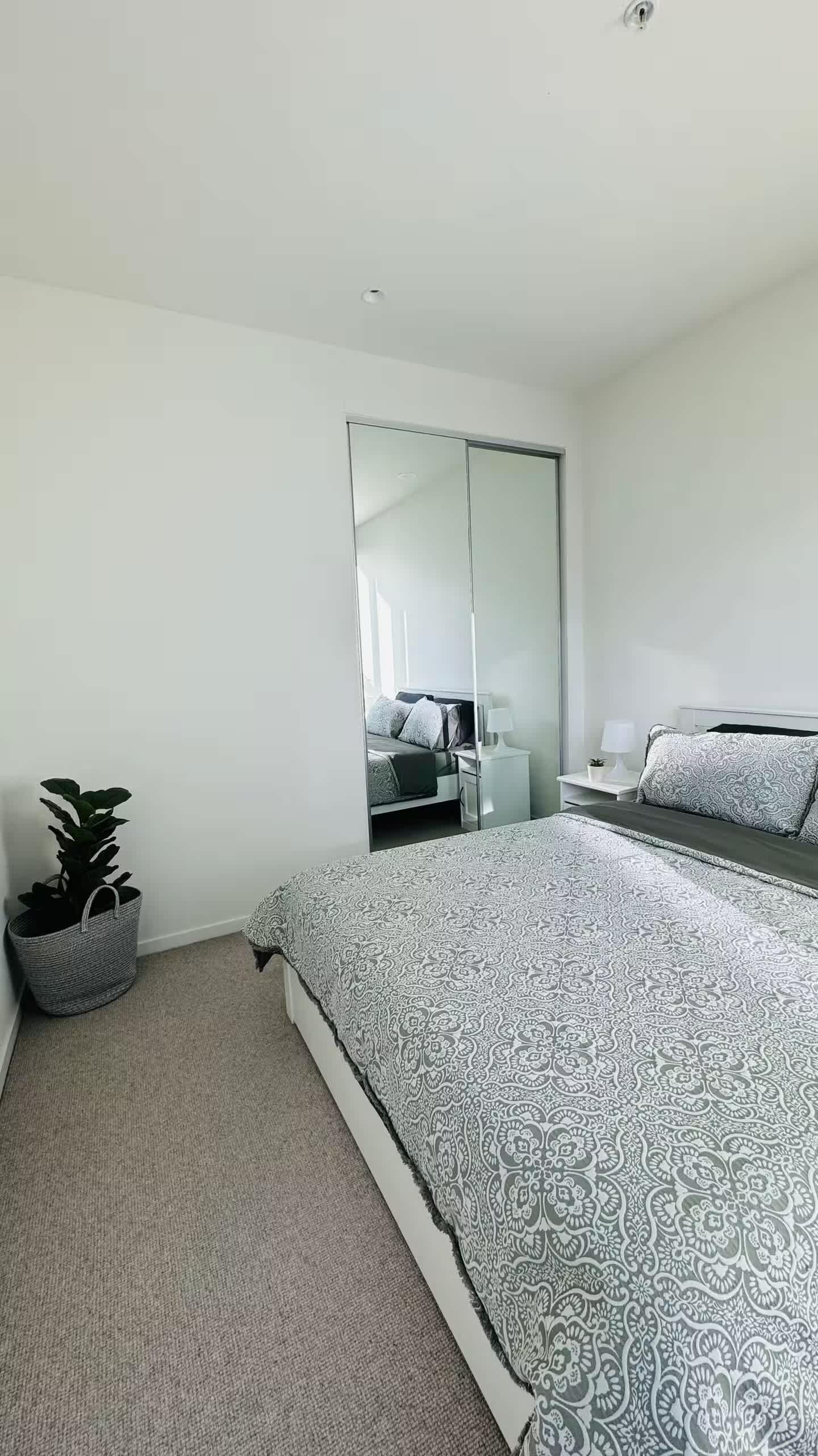 Ein modernes Schlafzimmer mit einem großen Bett, einem Nachttisch, einem Spiegel und einer Zimmerpflanze.
