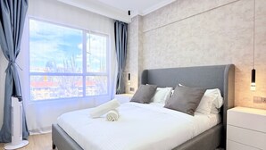 A modern bedroom with a large bed, a standing heater, a window with curtains, and a view of the outside. - Marina Bay Square Westlands (Nairobi)