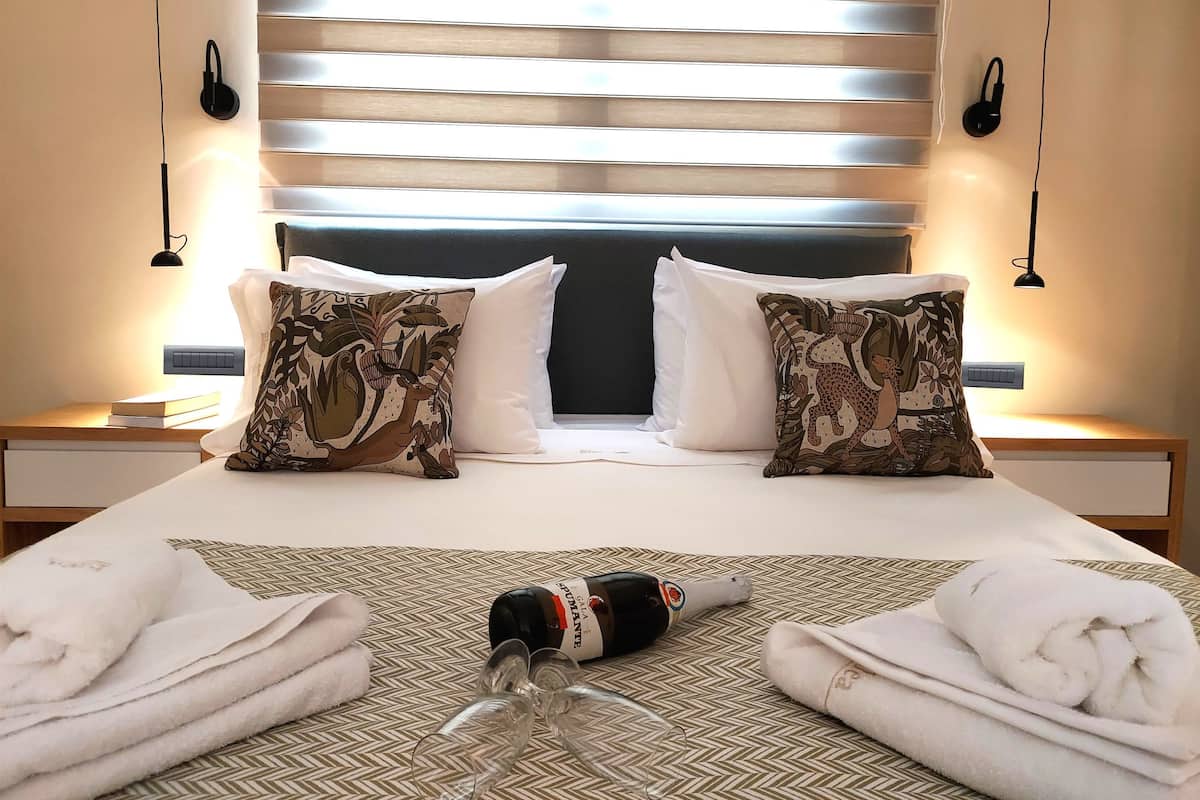 A hotel room with a bed, two pillows, a bottle, glasses, and towels.