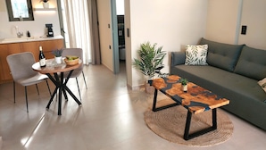 A modern living room with a sofa, a coffee table, and a dining area with a chair and table. - Elea Suites Adelianos Kampos (Rethymno)
