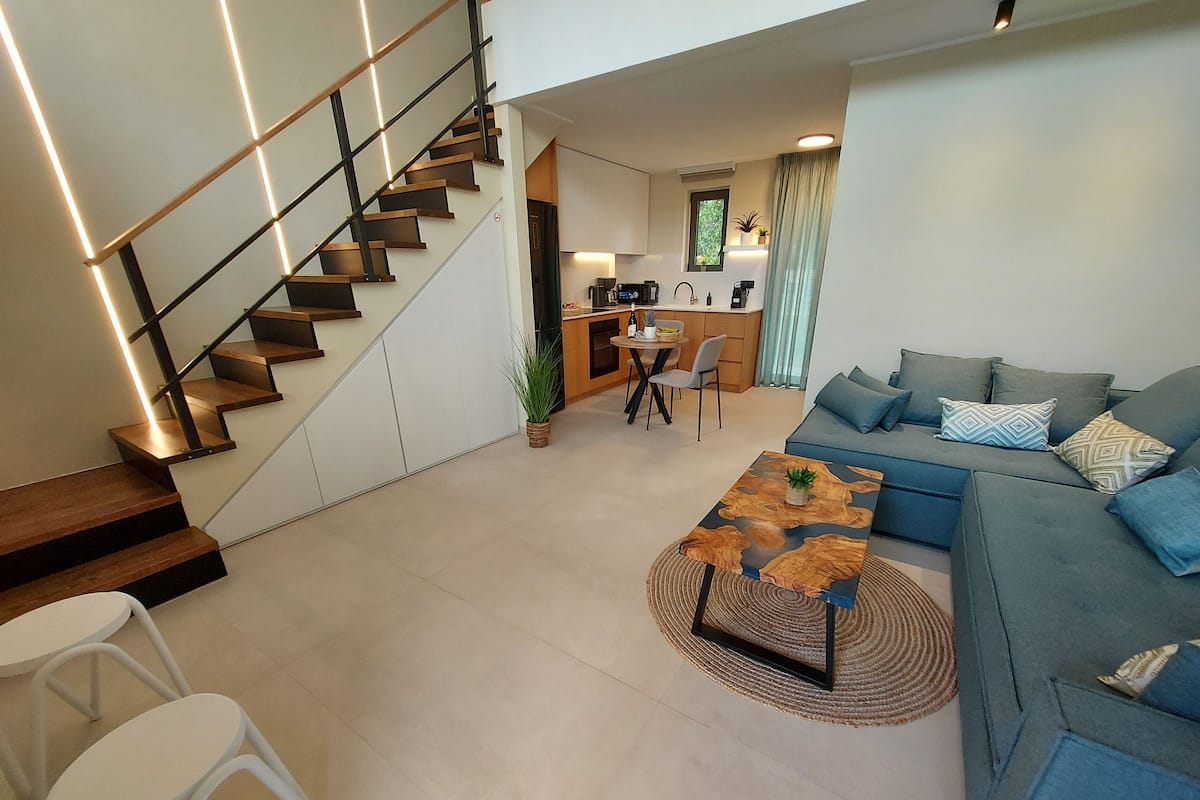 A modern living room with a staircase, a sofa, a coffee table, and a dining area.
