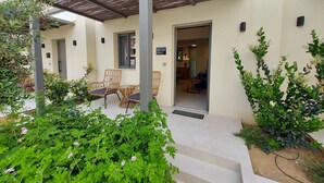 A covered outdoor seating area with wicker chairs, a small table, and a door leading to an interior space. - Elea Suites Adelianos Kampos (Rethymno)