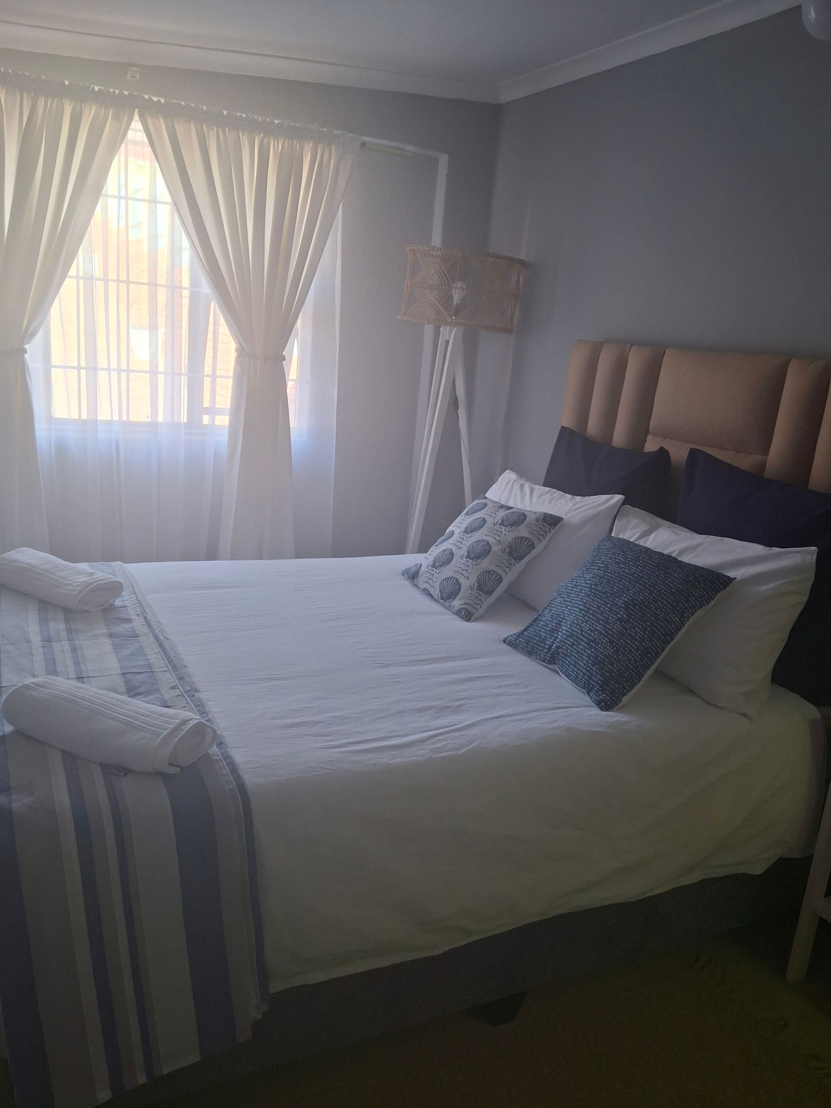 A neatly made bed with pillows and a striped blanket, a bedside lamp, and a window with curtains.