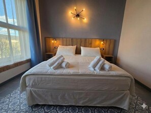 A hotel room with a large bed, a wooden headboard, bedside tables, and a wall-mounted light fixture.