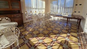 A room with a tiled floor, a dining table with chairs, a wooden cabinet, and a chandelier.