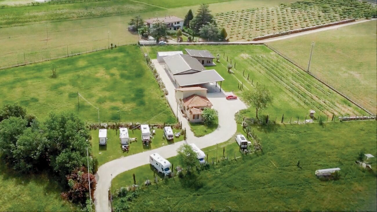 An aerial view of a rural property with a large building, multiple RVs, and surrounding fields.