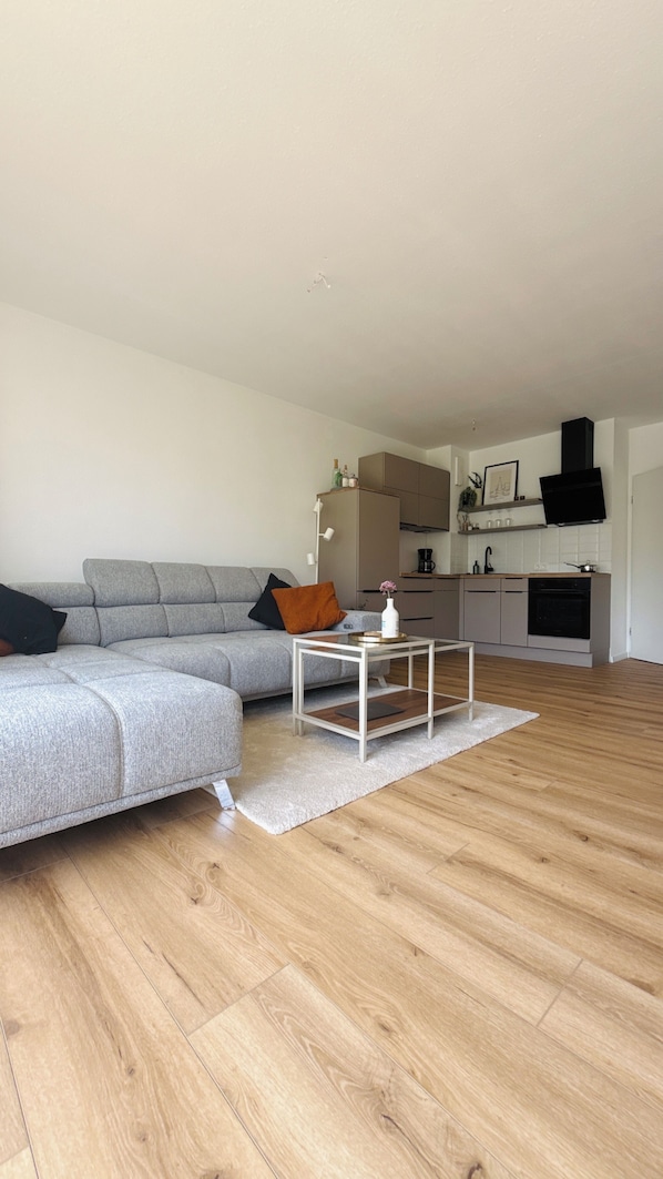 A living room with a grey sofa, a white coffee table, and a kitchen area with modern appliances.