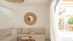 Ein modernes Wohnzimmer mit einer Couch, zwei Holztischen, einem runden Spiegel und Blick auf eine Terrasse.