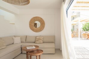 Ein modernes Wohnzimmer mit einer Couch, zwei Holztischen, einem runden Spiegel und Blick auf eine Terrasse.