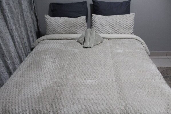 A bed with a textured blanket, two pillows, and a folded towel.